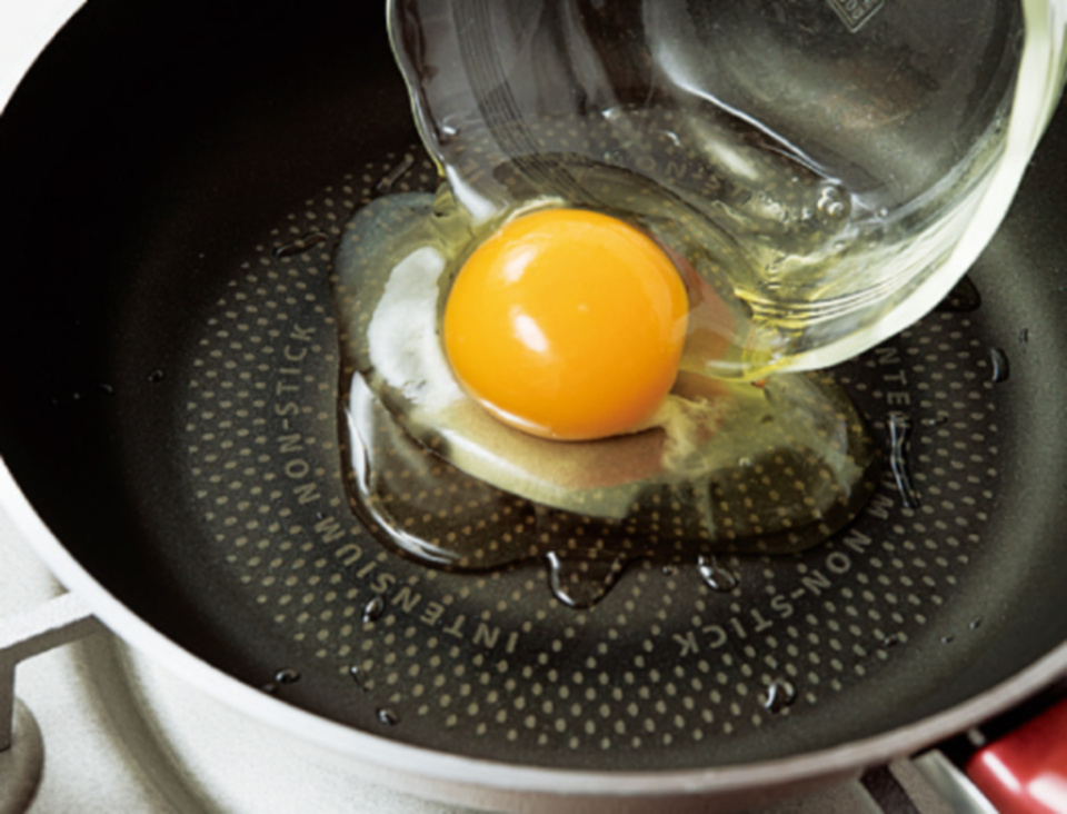 在平底鍋裡倒油，以中火加熱，敲碎蛋殼放進鍋裡。